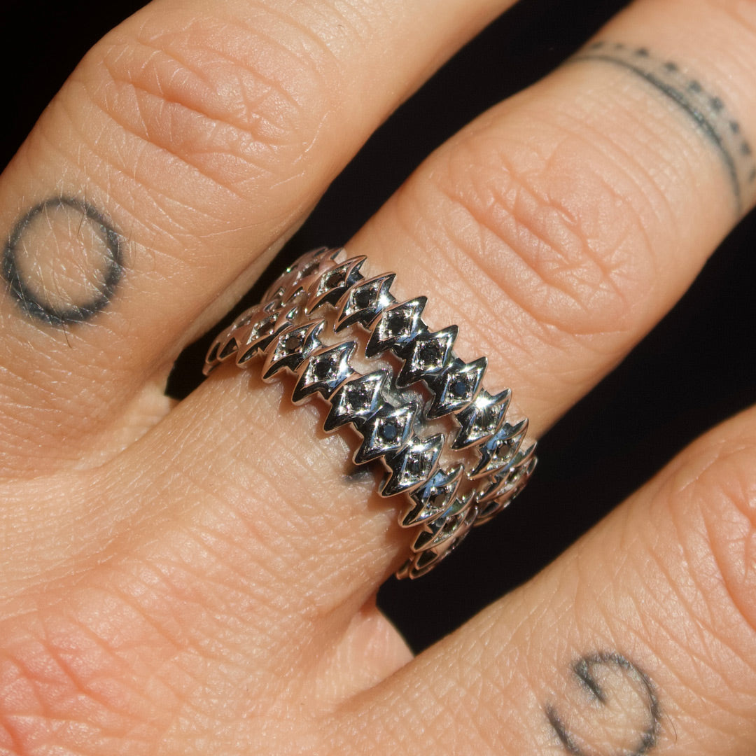 White gold star-shaped rings with black diamonds on a finger with tattoos