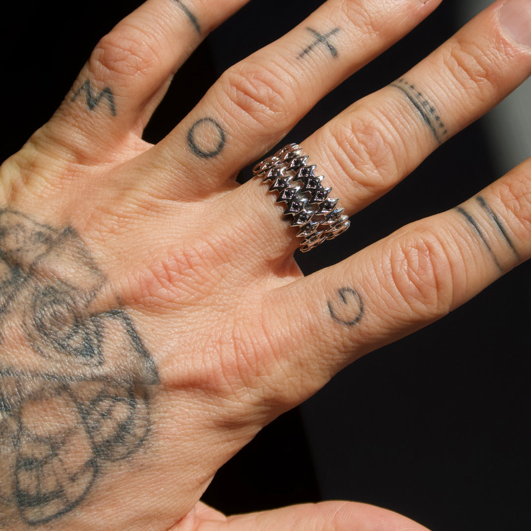 Hand with tattoos wearing a spiked rings on a dark background