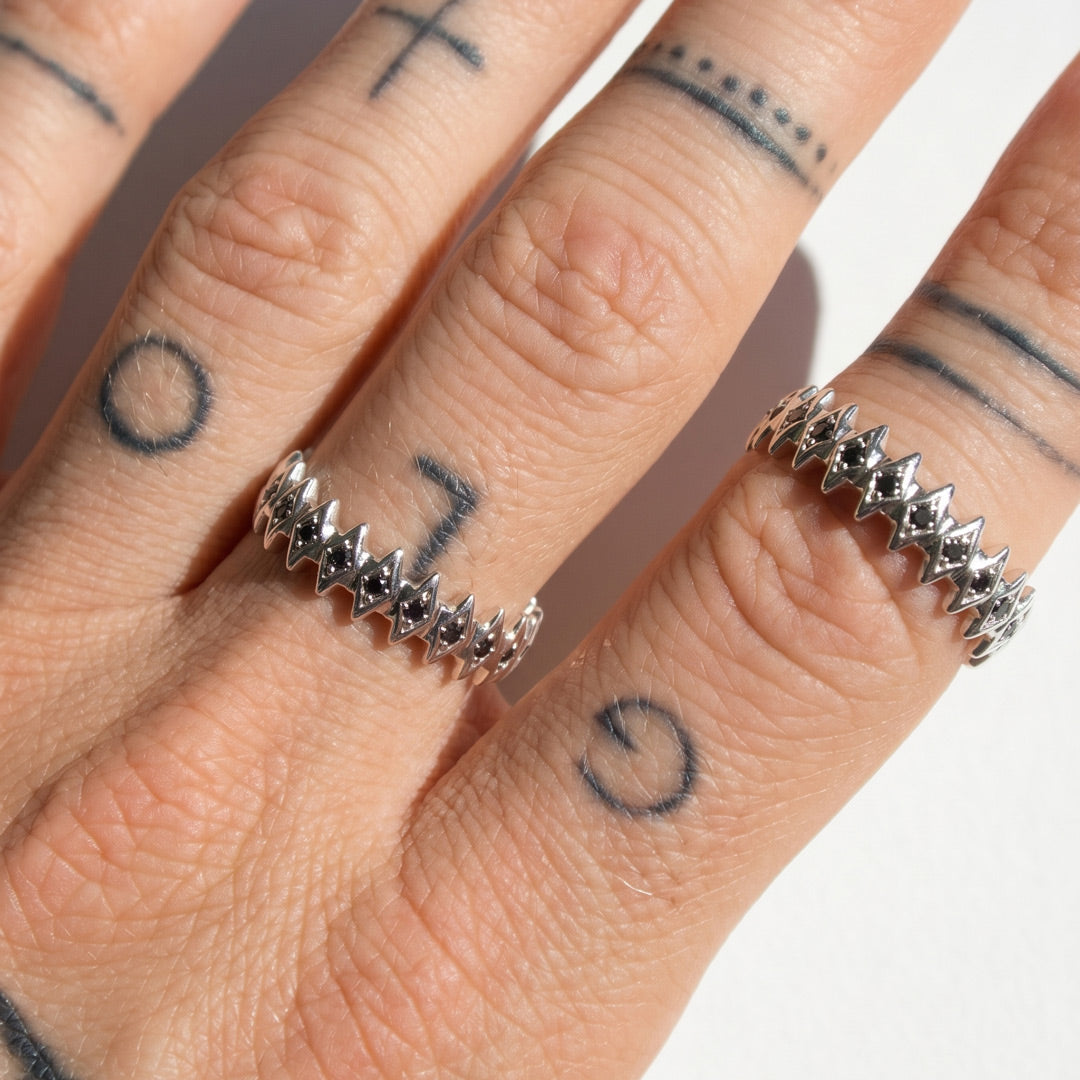 Close-up of a hand wearing two white gold rings with star designs on fingers with tattoos.
