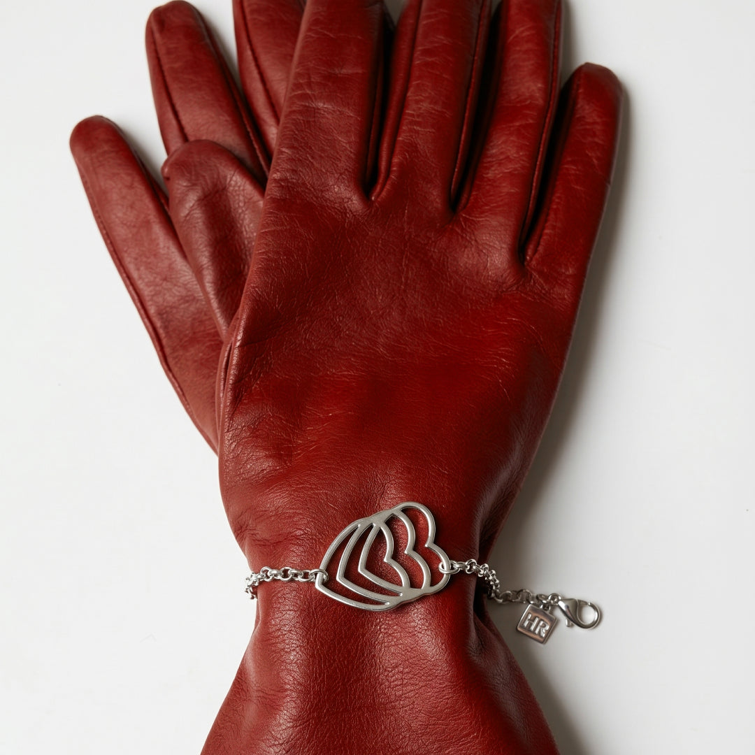 Red leather gloves with a silver bracelet featuring a heart design on a white background