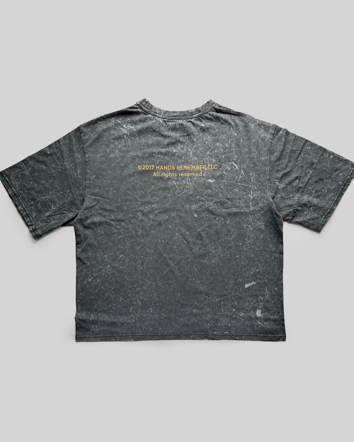 Gray t-shirt with yellow text on the back against a gray background