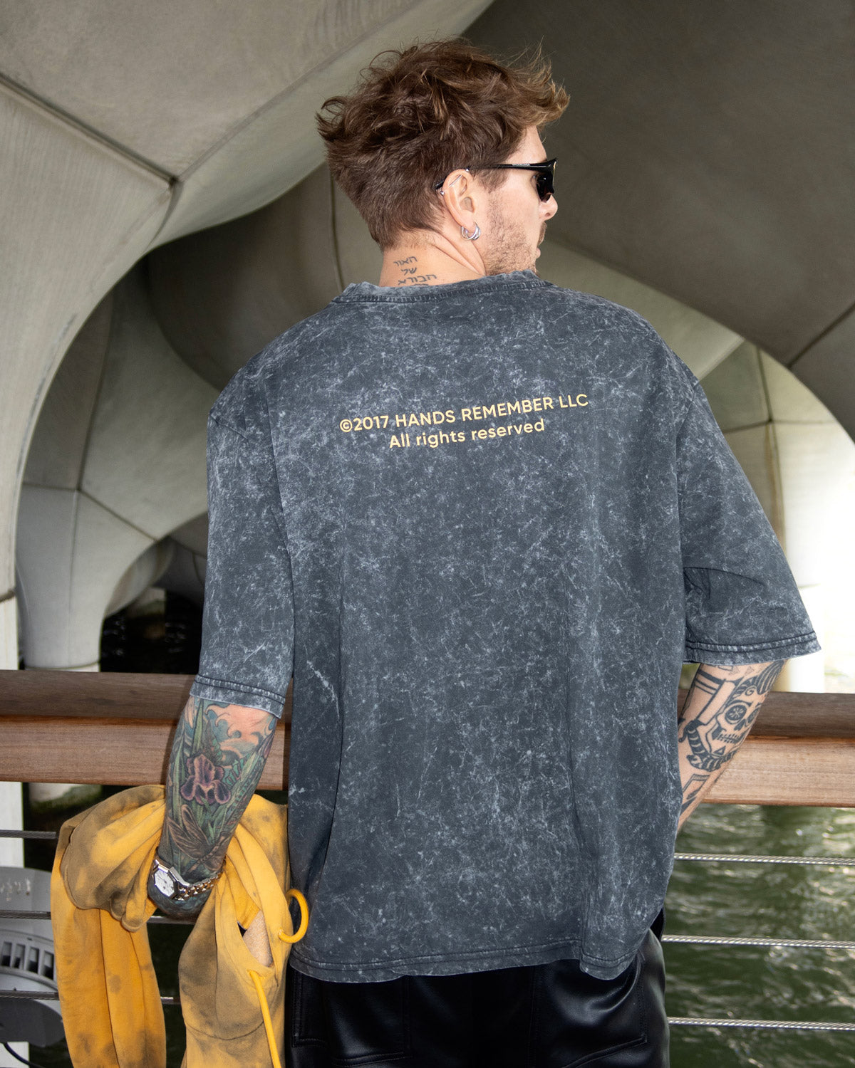 Oscar Renkel is wearing a dark gray t-shirt with text on the back, standing by a waterfront