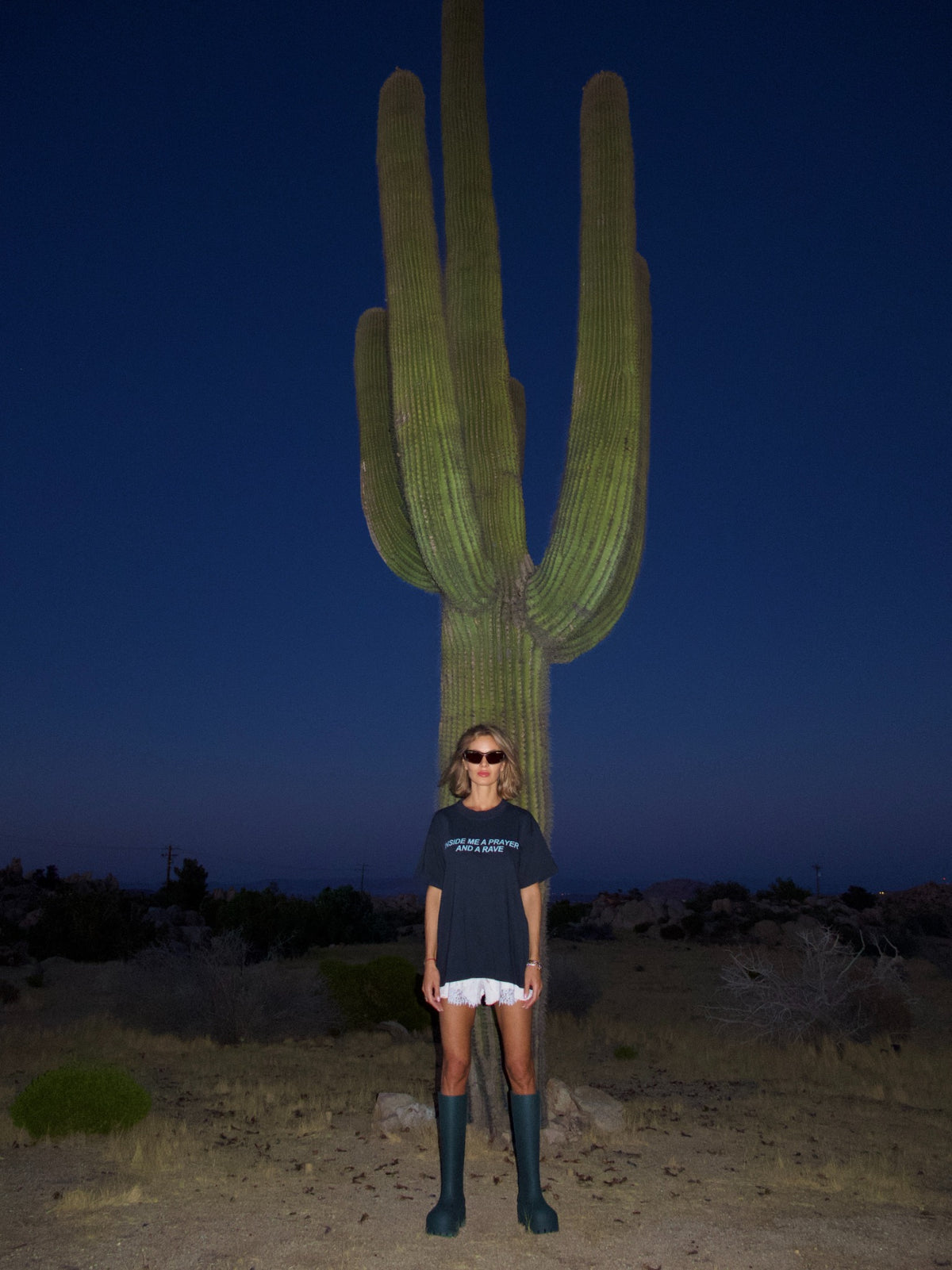 Black T-shirt with the “Inside Me a Prayer and a Rave” print, outdoor front view by a cactus.